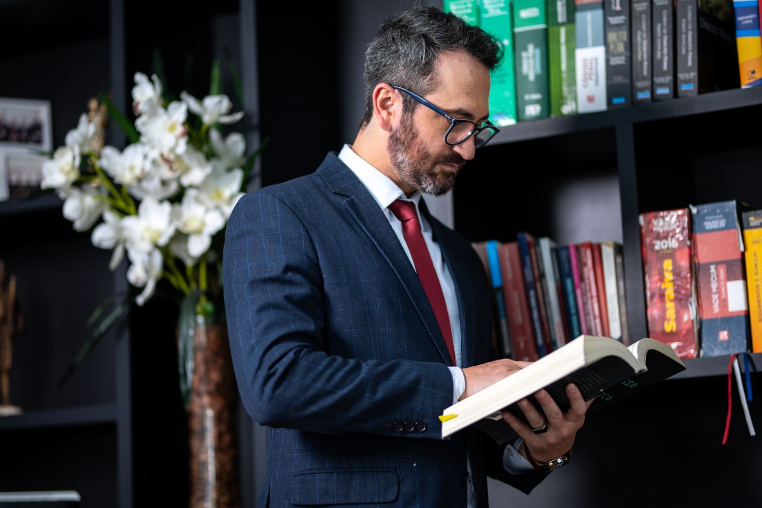 Roger Ellwanger lendo um livro jurídico em frente à estante do escritório