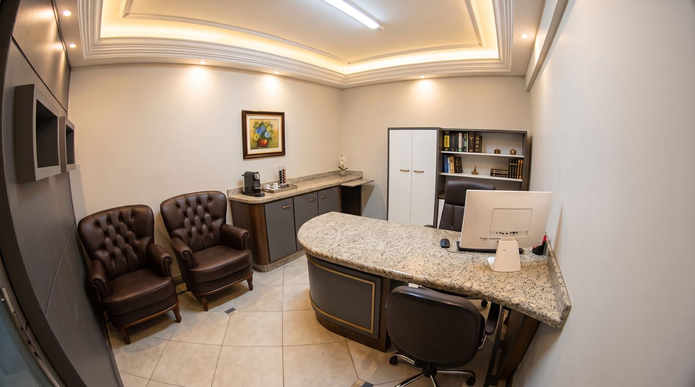 Sala de atendimento com poltronas, mesa de granito e estante